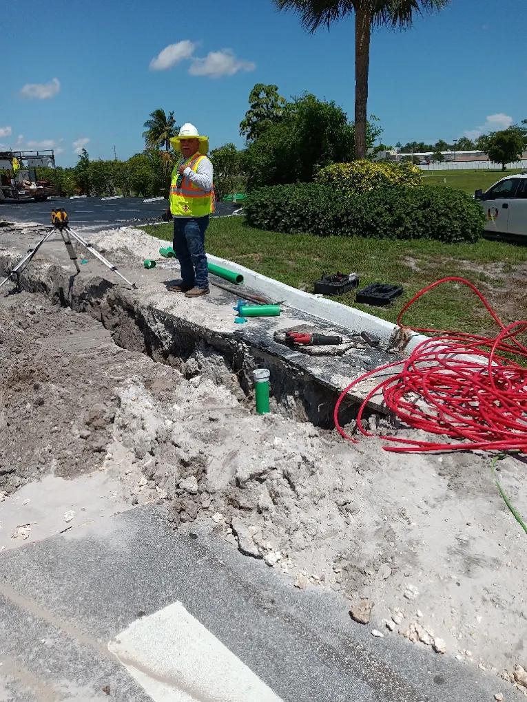 Worker beside exposed piping in an excavated trench