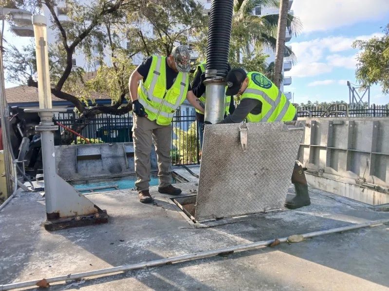 Two workers in safety vests servicing an open lift station access chamber